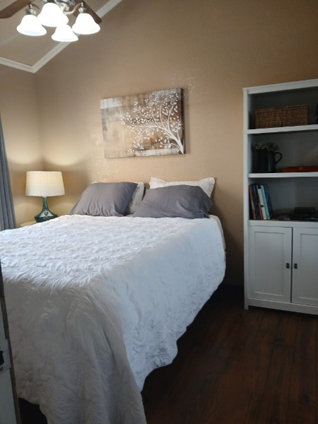 Furnished bedroom at Dennis Cottage in Kerr County, Texas, with vaulted ceiling, ceiling fan, wood flooring and bookcase.