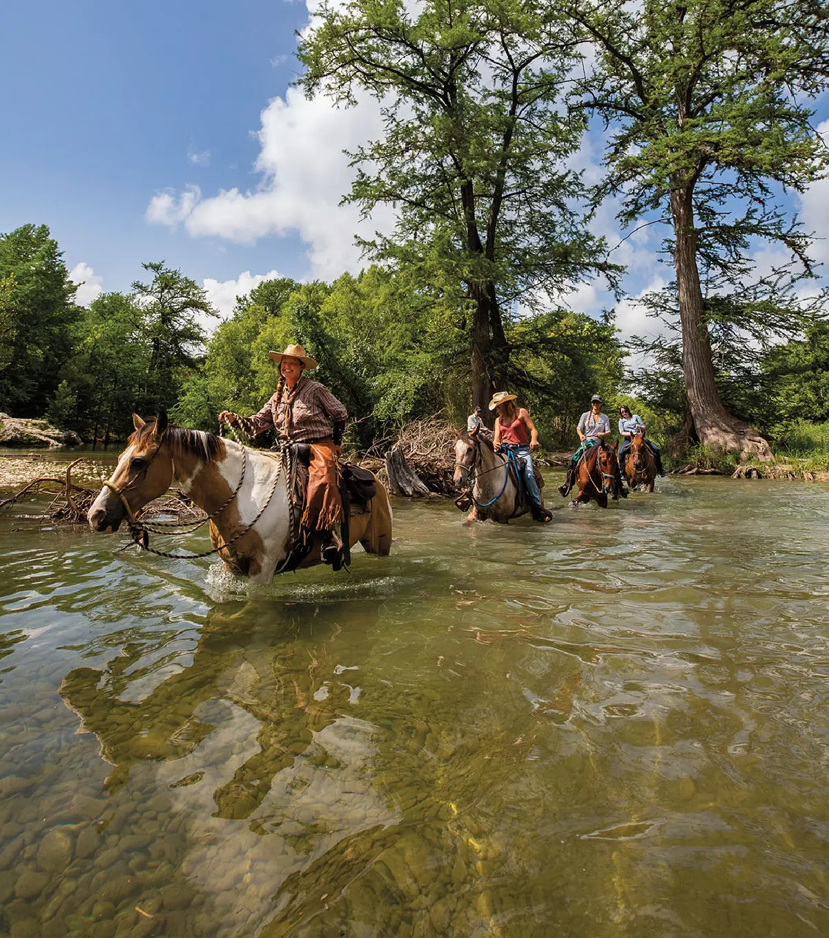 Riders on horseback crossing the clear, cypress-lined Medina River near Bandera, Texas, the Cowboy Capital of the World in the Texas Hill Country